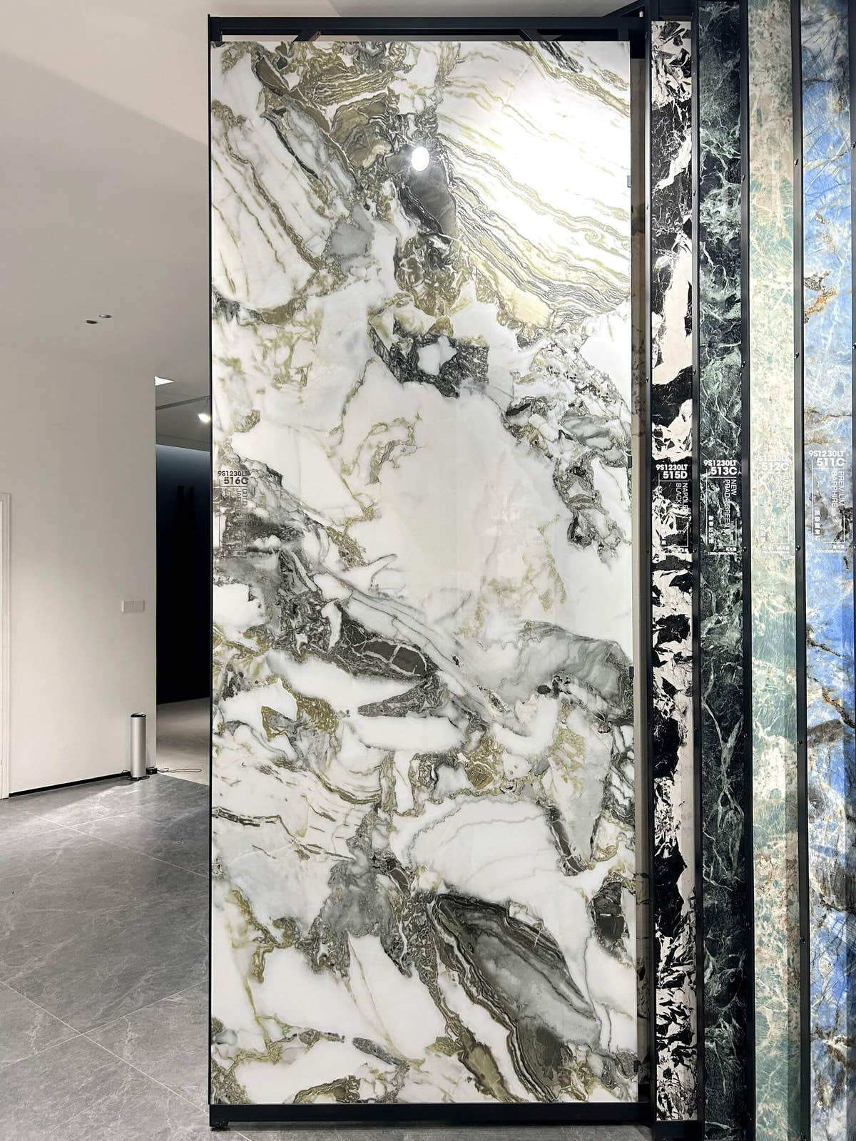 White, olive-green and dark grey veined slab on a showroom rack — Cold Jade Green sintered stone