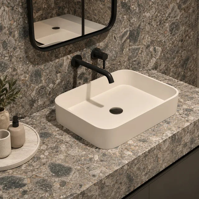 Encimera de baño y paneles murales de piedra sinterizada con aspecto de brecha, con un lavabo sobre encimera de color marfil; ilustración de uso generada con IA