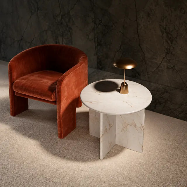 Mesa auxiliar redonda blanca veteada con una lámpara de latón junto a un sillón color óxido; imagen de referencia mejorada con IA