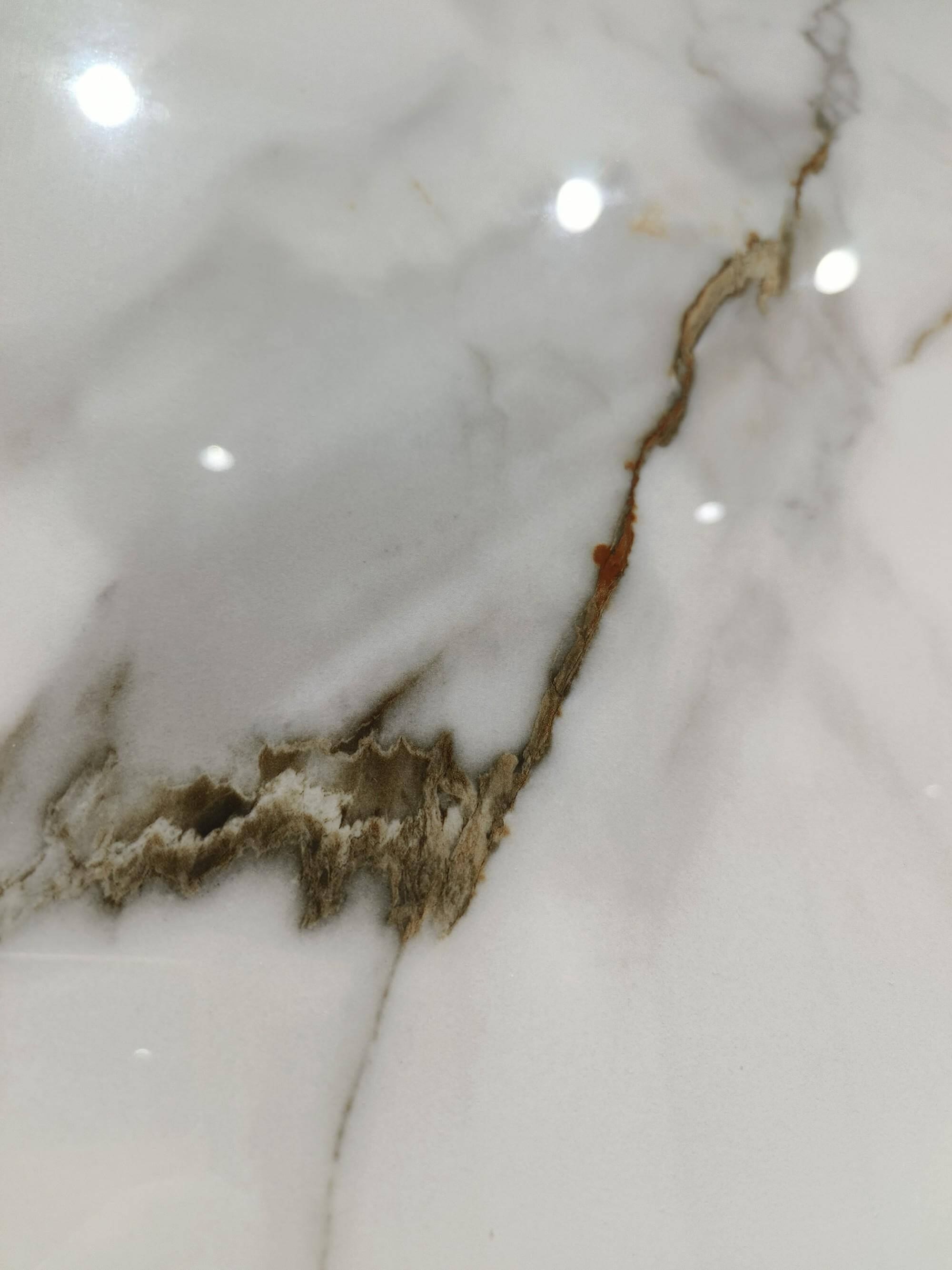 Крупным планом плита из спеченного камня Calacatta Gold Marble Look, демонстрирующая прожилки под мрамор и детали поверхности.